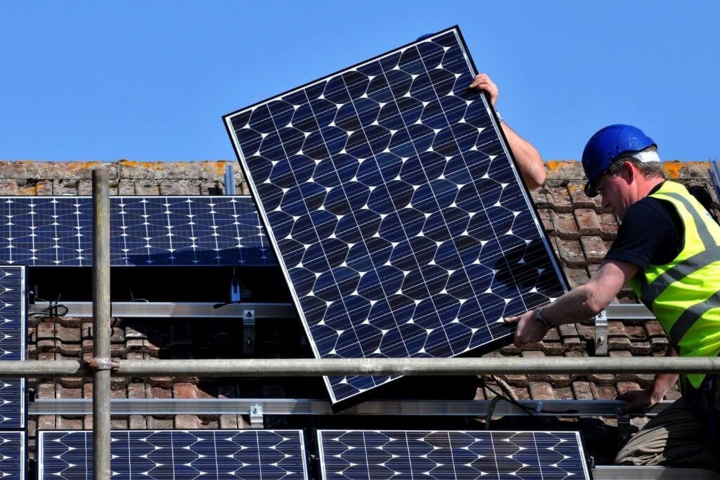 A contractor fits solar panels on the roof of a house.