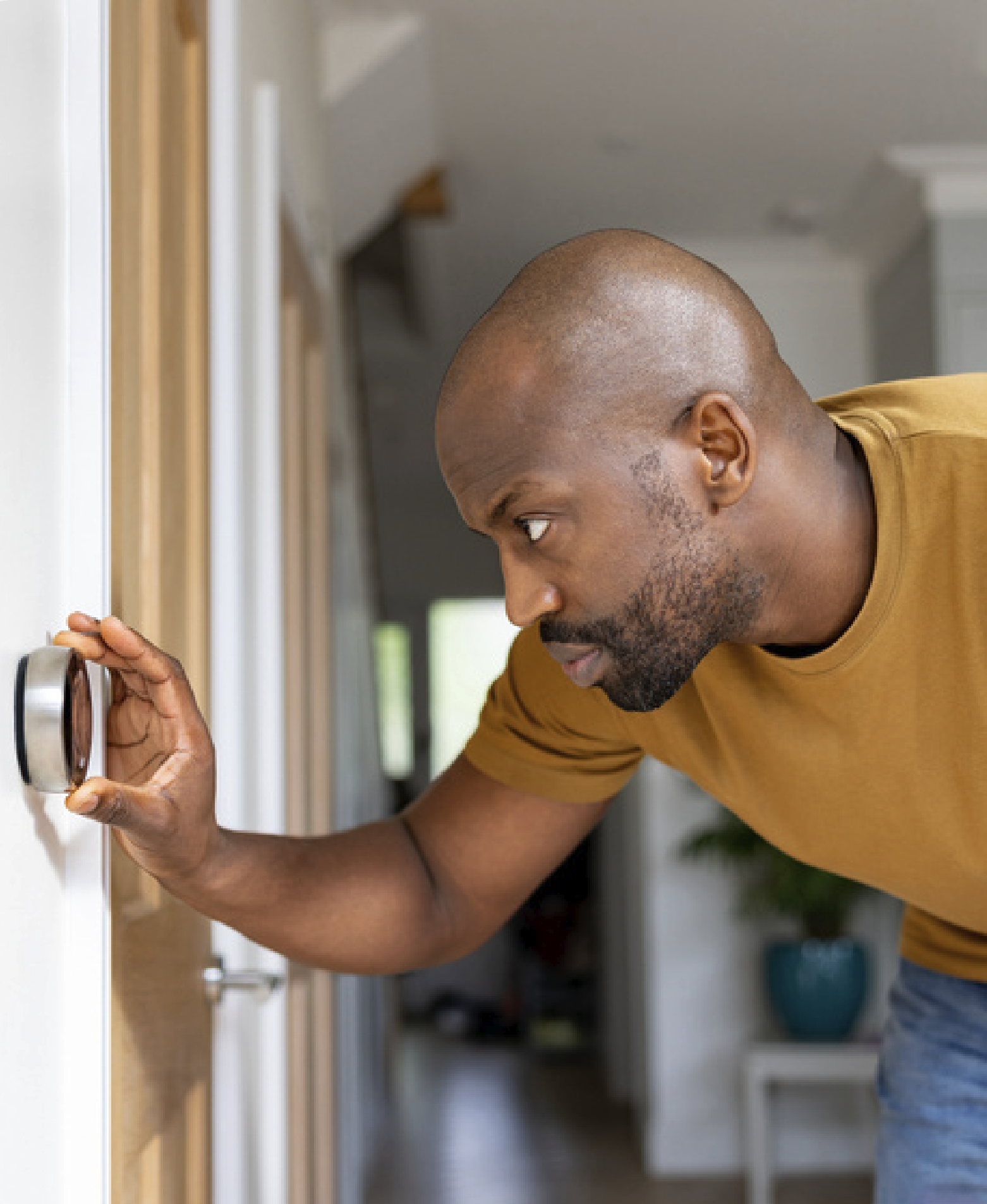 A close up of a man wearing a yellow t shirt adjusting the dial to a modern heating system in a home
