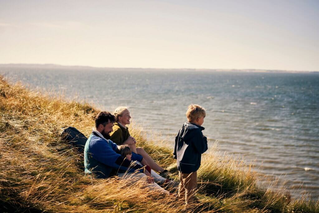 Young family sitting on a hillside looking out to sea smiling