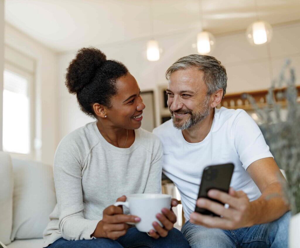 Couple at home looking at each other smiling with a cup of tea and a mobile phone