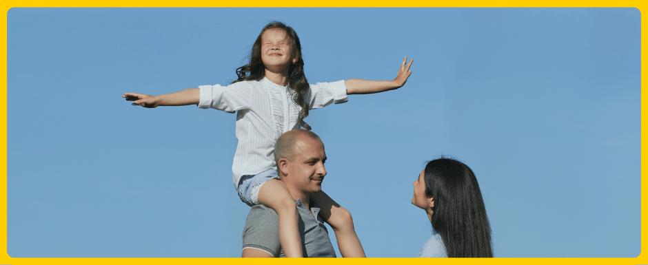 Small girl sitting on her father's shoulders as he talks to a woman