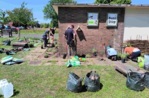 Volunteers planting flowers and greenery around a small brick building in an urban green space as part of a community improvement project